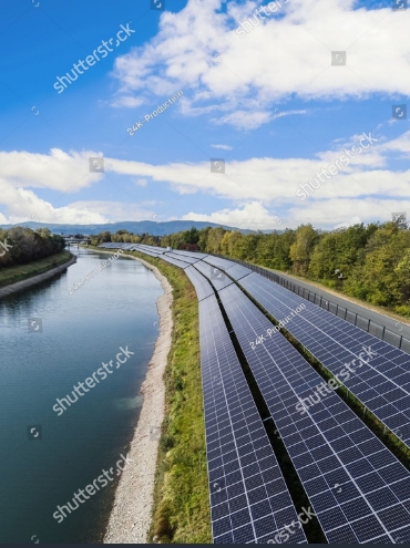 stock-photo-solar-panels-are-set-up-along-the-river-bank-with-trees-and-mountains-in-the-background-under-clear-2731701609